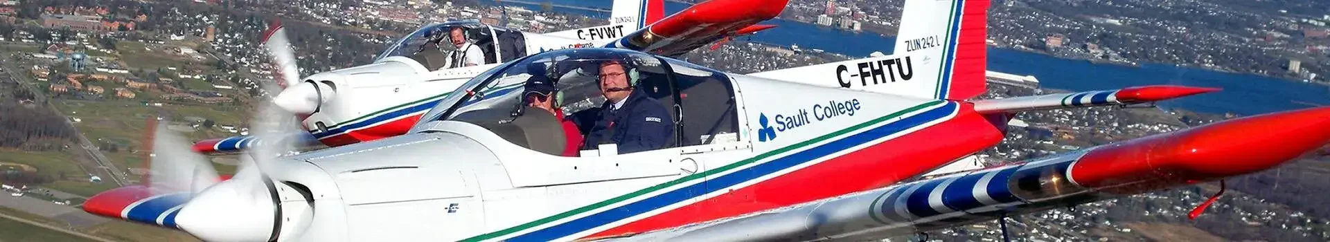 2 small planes side by side in the air with pilots inside