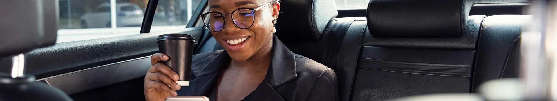 Woman holding coffee smiling in back seat of a taxi